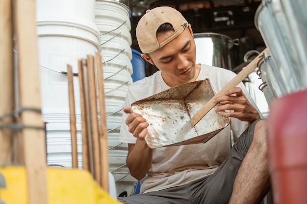 Asian male seller holding a dustpan trash when sitting on the floor in the household appliances store