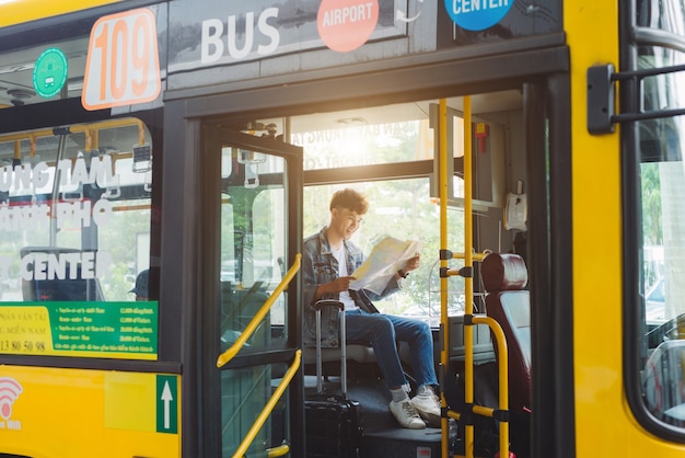 asian male tourist sitting in city bus and reading a map.