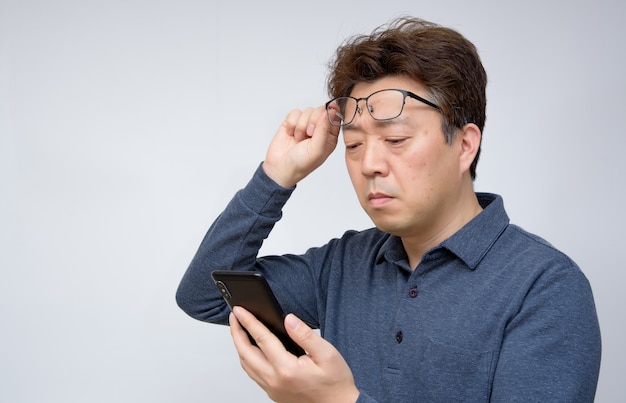 Азиатский мужчина пытается прочитать что-то на своем мобильном телефоне. плохое зрение, пресбиопия, миопия.