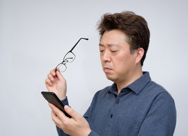 Asian male trying to read something on his mobile phone. poor sight, presbyopia, myopia.