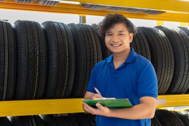 Photo asian male worker checking new tires wheels on the shelf at auto store shop and car repair service