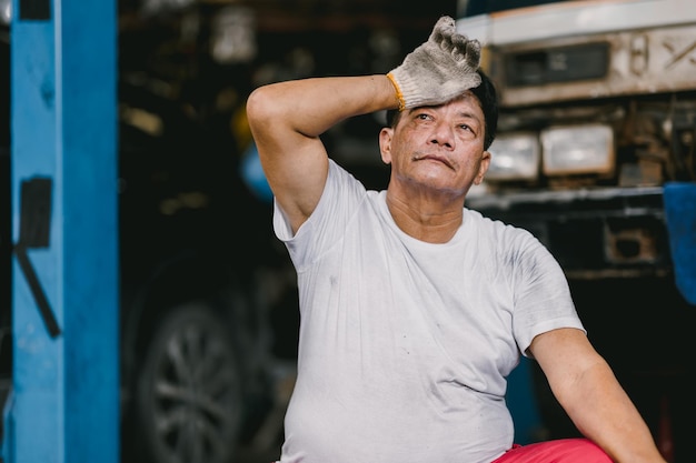 Lavoratore maschio asiatico stanco esausto affaticamento dovuto al duro lavoro nel posto di lavoro caldo e sporco cattivo benessere del lavoro