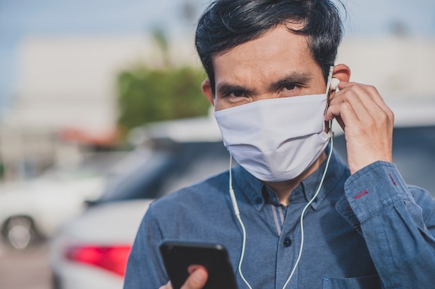 L'uomo asiatico è telefono di chiamata telefono usa la maschera in città