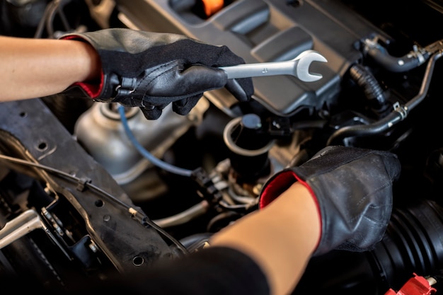 Asian man auto mechanic using a wrench and screwdriver to working service car in garage.