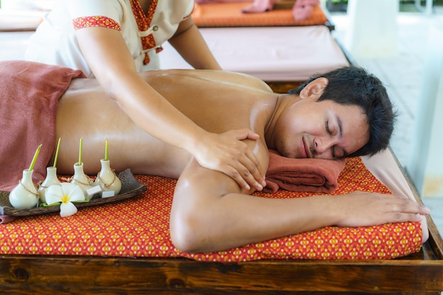 Uomo asiatico nel salone della spa sulla spiaggia che ottiene massaggio con olio vicino alla spiaggia e sembra felice in thailandia. concetto di spa, resort, bellezza e salute.