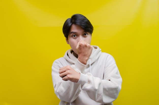 Asian man in beige hoodie dancing happily and raising his fist celebrating victory