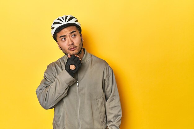 Asian man in bike helmet and gloves looking sideways with doubtful and skeptical expression