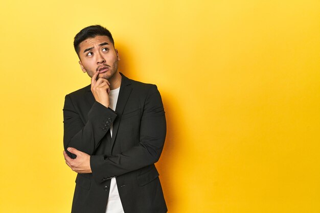 Photo asian man in black business jacket on yellow studio looking sideways