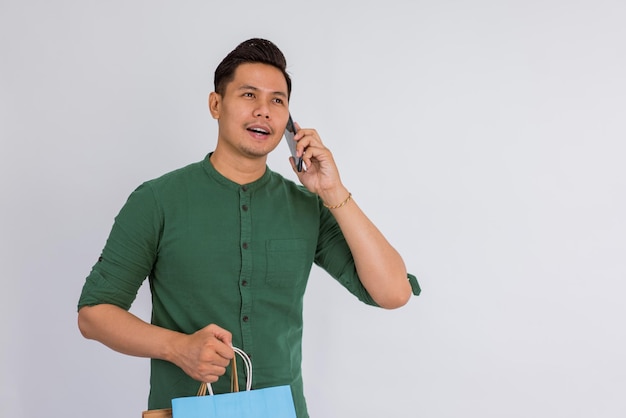 Asian man calling someone on phone while bring the shopping bags on isolated background