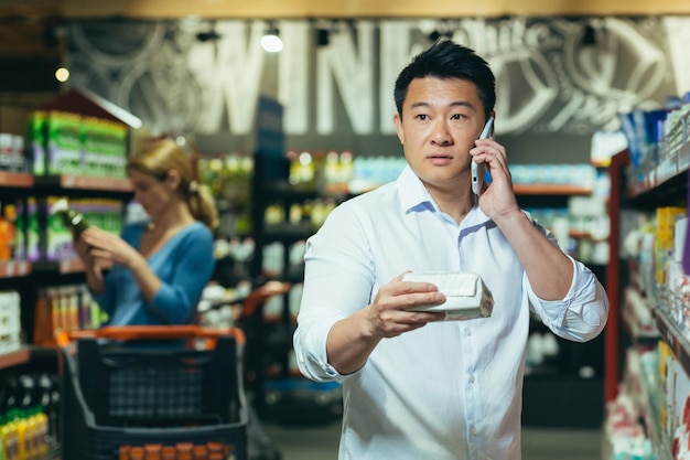 An asian man cannot choose a product in a supermarket has difficulty choosing calls his wife for