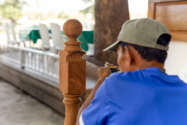 Carpentiere asiatico dell'uomo che tratta un di legno con lo scalpello all'aperto.