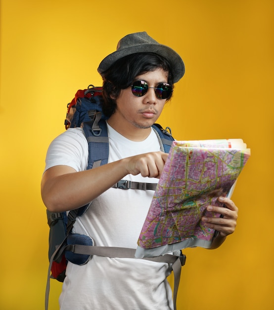 Asian Man Carrying Big Backpack Pointing a Map Against Yellow Background          