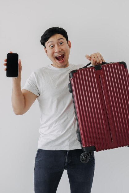 Asian man carrying a suitcase and holding mobile phone showing application for travel and booking