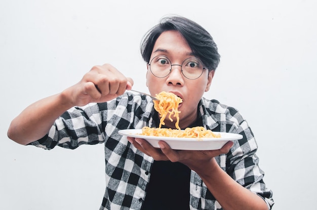 Asian man in casual shirt eats instant noodles using fork hungrily