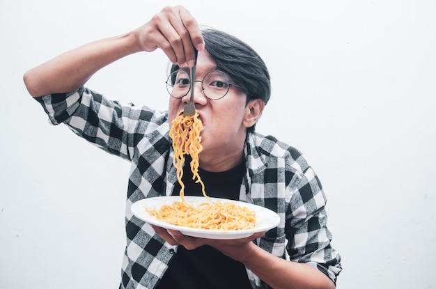 L'uomo asiatico in camicia casual mangia avidamente spaghetti istantanei usando la forchetta