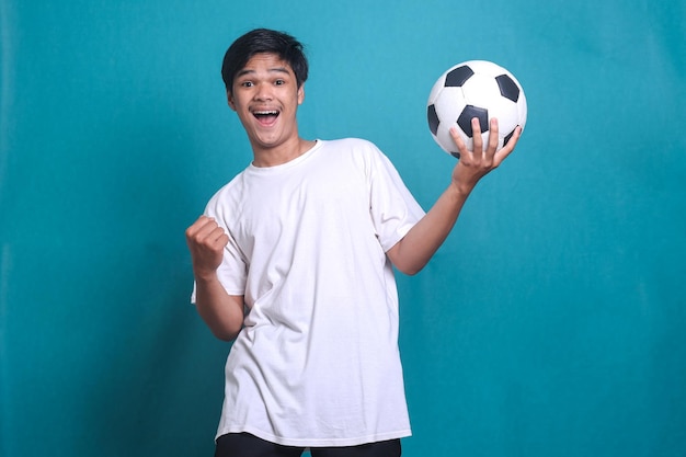 Asian man cheer up support favorite team hold soccer ball doing winner gesture