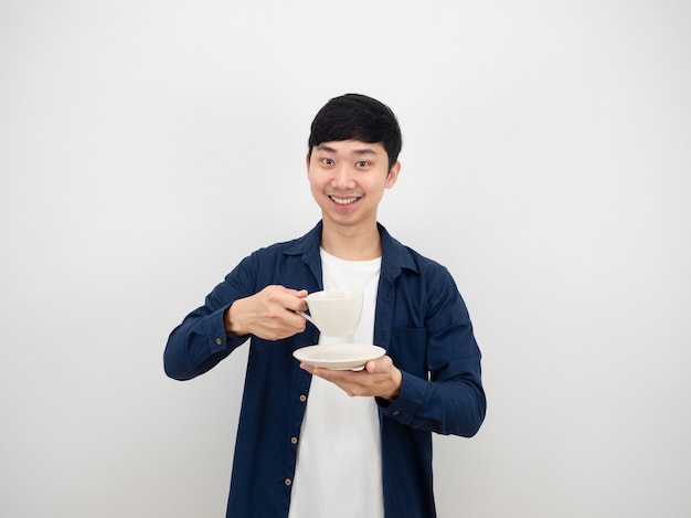 手にコーヒーカップを持って陽気で幸せな笑顔のアジア人男性白い孤立した背景の上のカメラを見てください