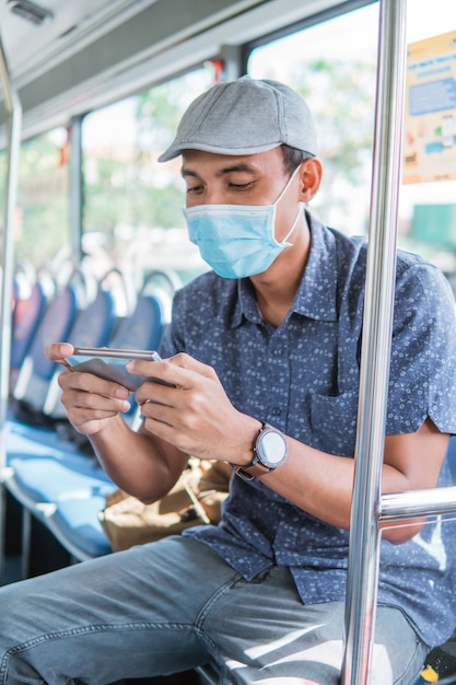 Uomo asiatico che fa il tifo e gioca sul suo telefono cellulare mentre guida nel trasporto pubblico