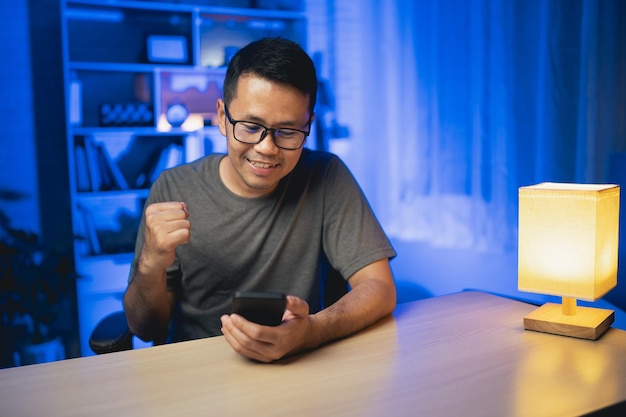 Asian man cheering sports while watching mobile phone live smiling and happy Asian man smiling and happy to win a bet Cheering for the success of the concept