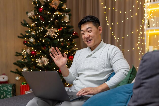 Asian man on christmas at home talking on video call sitting on sofa in living room near christmas