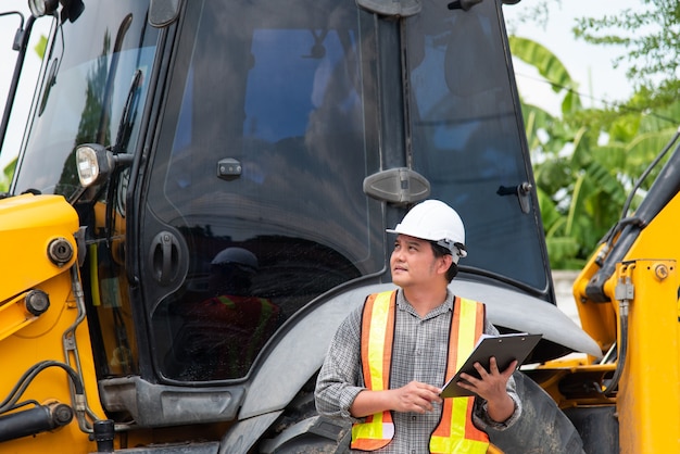 Asian man civil construction engineer worker or architect with helmet and safety vest working and holding a paper board note for see blueprints or plan at a building or construction site