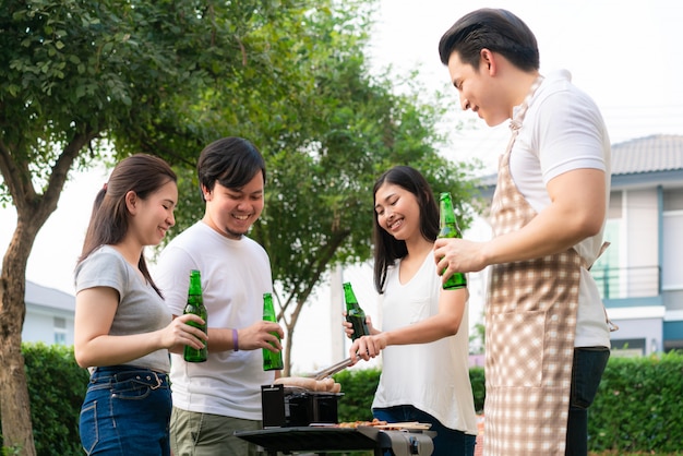 Asian man cooking barbeque grill and sausage for a group of friends to eat party in garden at home.