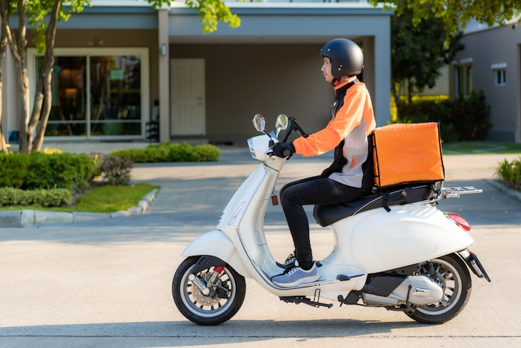  Asian man courier on scooter delivering food in town streets with a hot food delivery from take awa