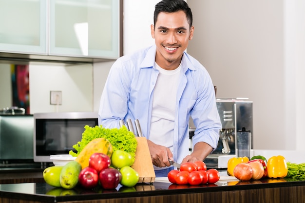 Asian man cutting salad in kitchen