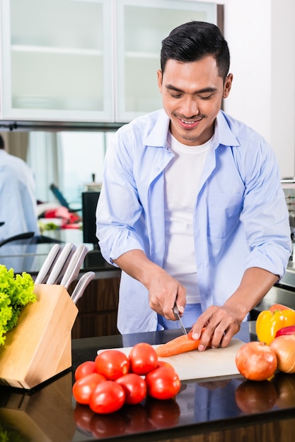 Asian man cutting vegetables in domestic kitchen preparing salad