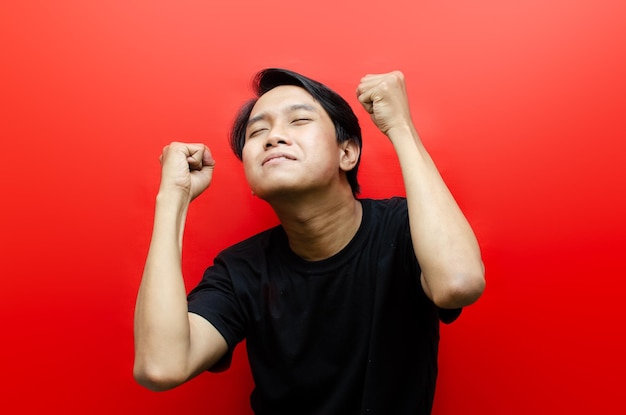 Азиатский мужчина счастливо танцует жестом руки "да", празднуя хорошие новости, изолированные на красном фоне