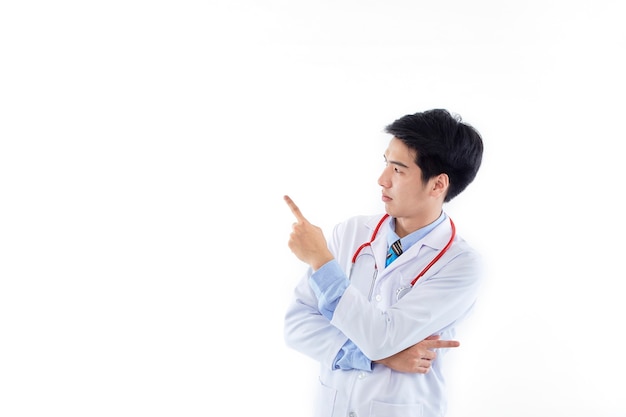 Asian man doctor in a medical gown stethoscope pointing index fingers aside on copy space  isolated on white wall
