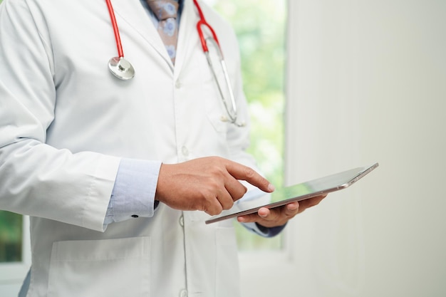 Asian man doctor using tablet computer to reading patient report check up and search for solve