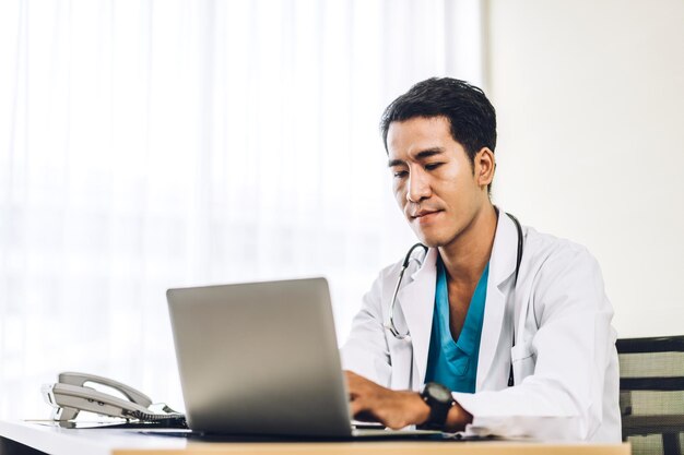 Asian man doctor wearing uniform with stethoscope working with laptop computer in hospital.healthcare and medicine