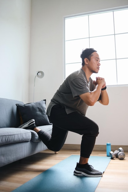 Asian Man Doing Single Leg Split Lunge Near Sofa At Home