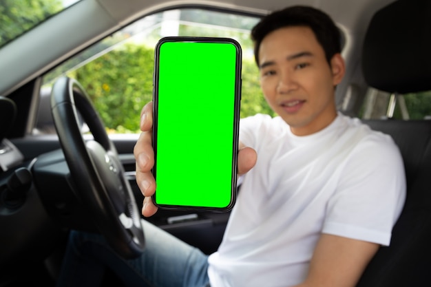 Autista asiatico dell'uomo che si siede nell'automobile e che tiene telefono cellulare con il fondo di schermo verde