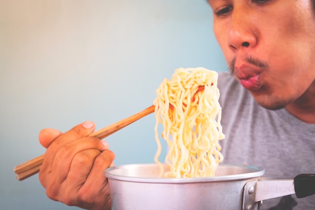 Asian man eating instant noodles in pot
