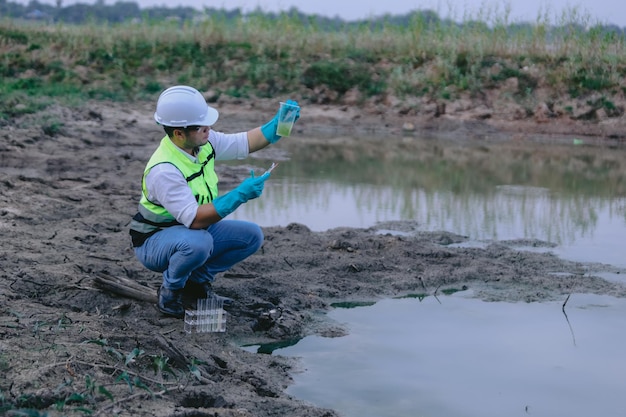 Азиатский эколог держит увеличительное стекло, чтобы осмотреть воду в прозрачном стекле на озере