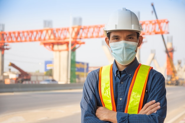 La maschera facciale asiatica dell'operaio dell'ingegnere dell'uomo che sta sulla costruzione del sito, il cappello duro di architettura protegge il controllo dell'operaio