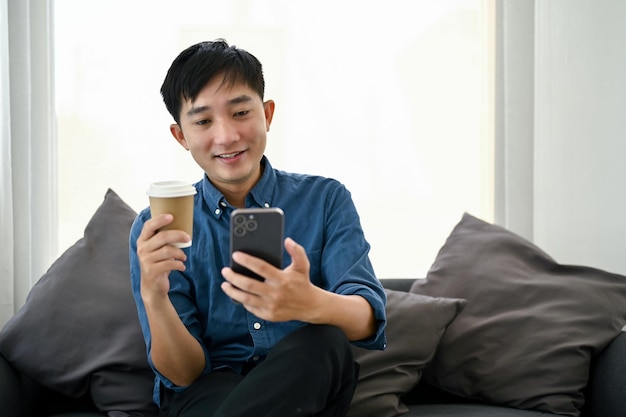 An Asian man enjoying his coffee while scrolling on his phone at a living room