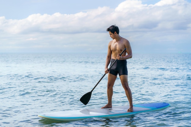 Asian man exercising sup board in turquoise tropical clear waters in summer day.