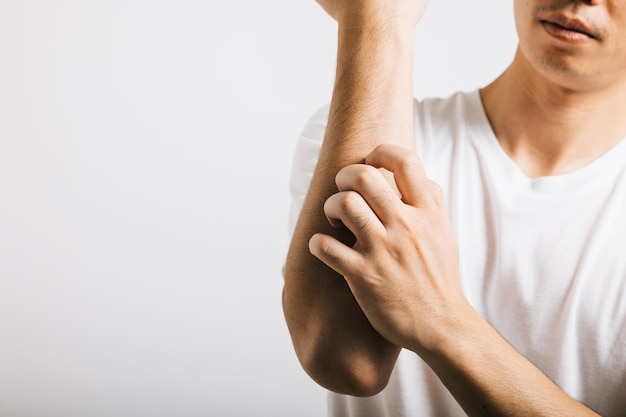 Asian man experiences itchiness on his arm possibly due to a mosquito bite Studio shot isolated on white background depicting discomfort and allergy symptoms like dermatitis and scabies