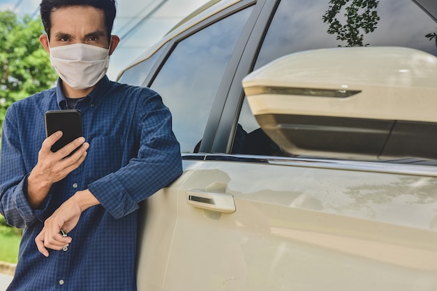 Asian man in facemask holding phone standing at car