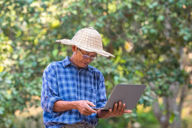 Coltivatore asiatico dell'uomo con il concetto di affari e tecnologia del computer portatile e dello smart phone, agricoltore asiatico dell'uomo sullo spazio vuoto della copia