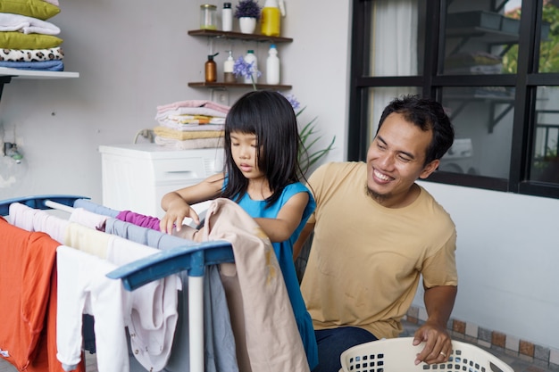 Азиатский мужчина отец домохозяин и дочь ребенка в прачечной сушке одежды