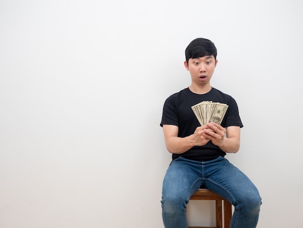 Asian man feeling amazed with money in his hand say wow sitting on chair white background