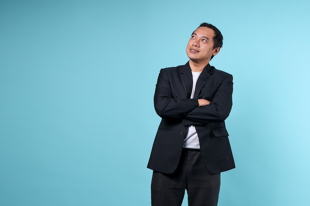 Азиатский мужчина в формальном костюме работает в офисе, глядя вверх, чтобы скопировать пространство, изолированное на синем фоне