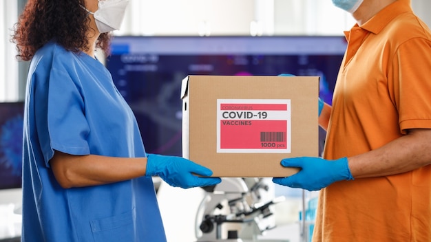 병원에서 아시아 간호사에게 코비드 19 백신 상자를 다루는 아시아 남자. Covid 19 예방 접종에 대한 개념입니다.