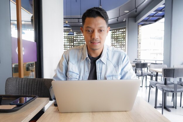 Asian man happy and smile face using laptop and mobile phone in coffee shop online