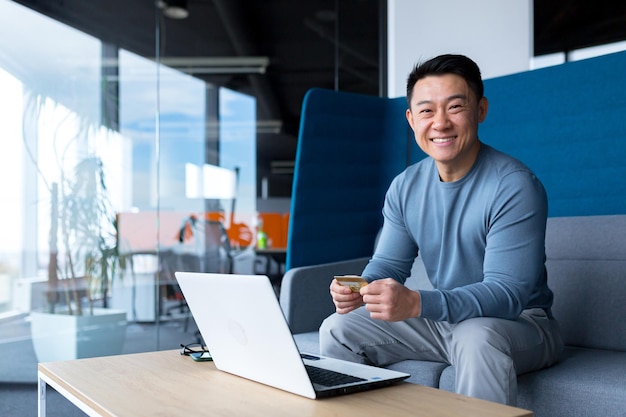 Asian man happy and smiling, businessman looking at camera and holding credit card for shopping in online stores