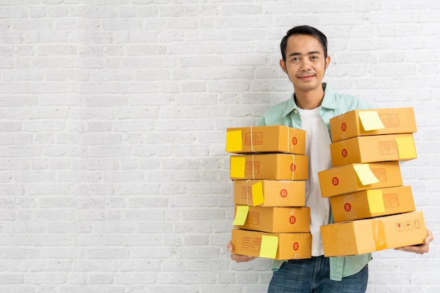 Asian man holding carry brown parcel or cardboard boxes on brick wall